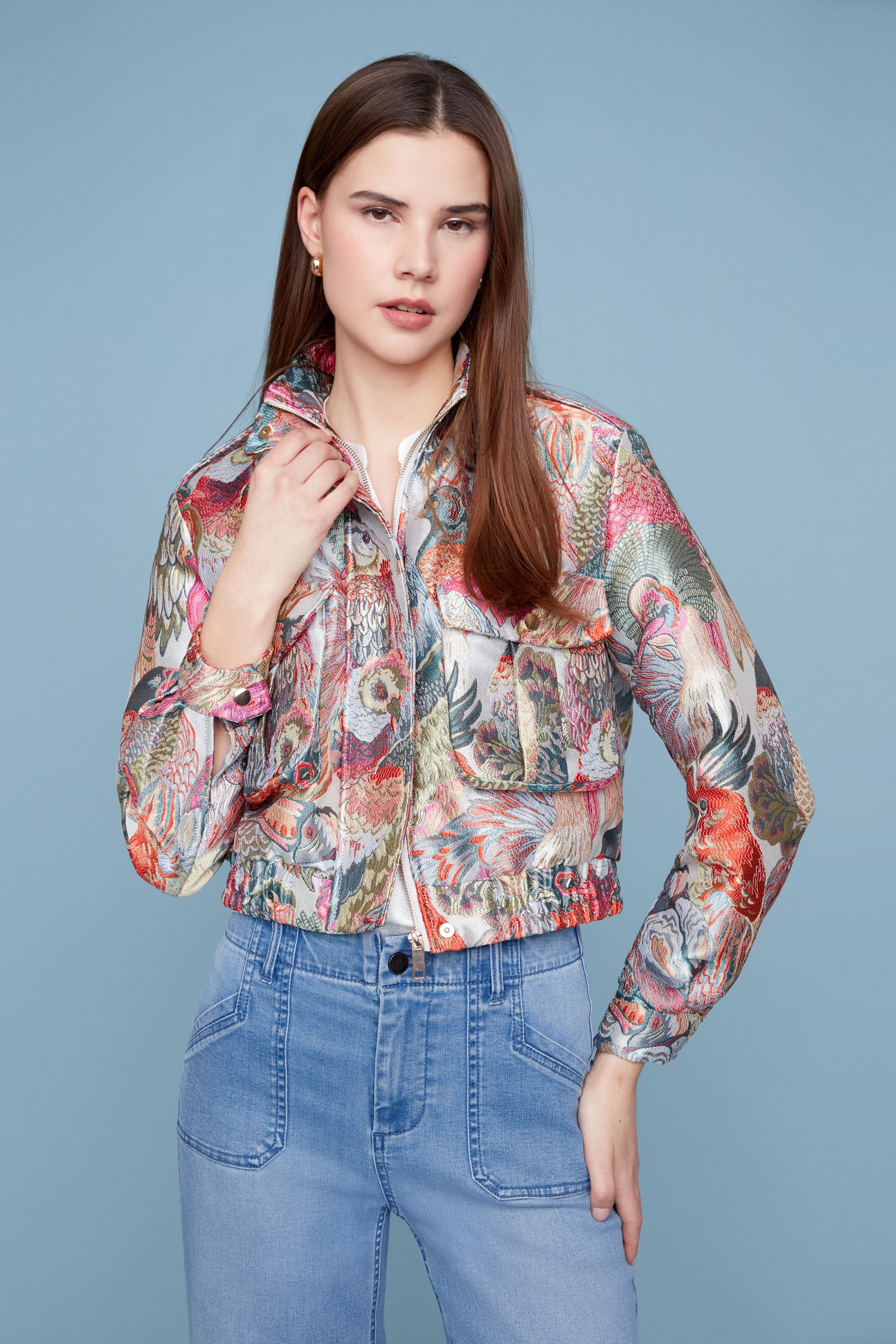 Woman wearing a colorful floral jacket and blue jeans against a light blue background